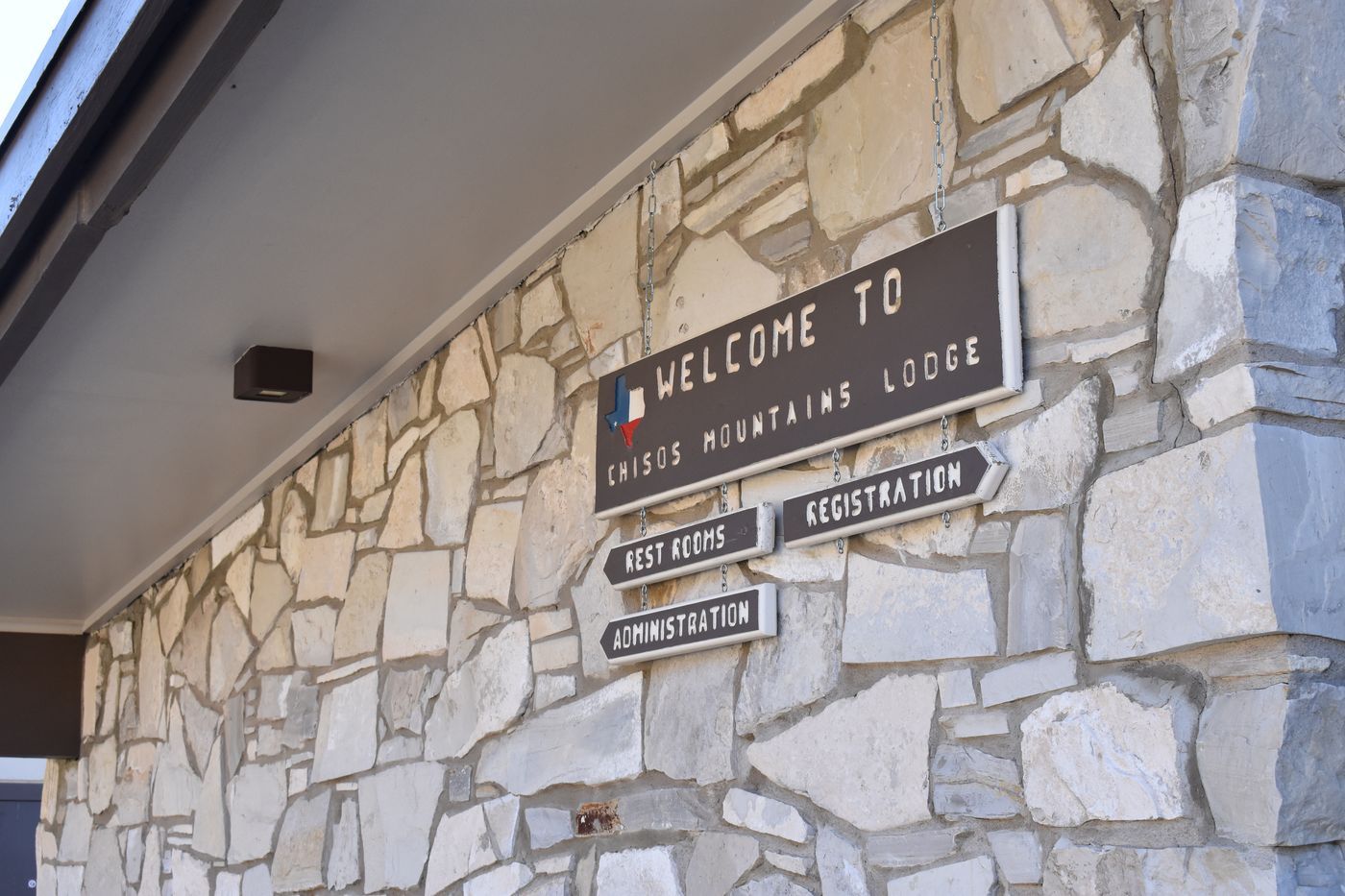 A wooden Welcome to Chisos Mountains Lodge sign on a stone wall, with arrows to registration and administration