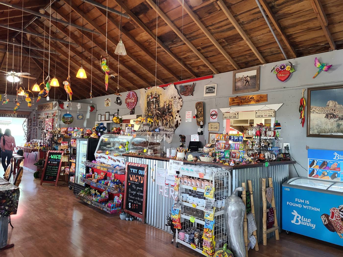 The counter and glass pie case inside May's Cornudas Cafe, under open wood rafters hung with brightly painted carved birds