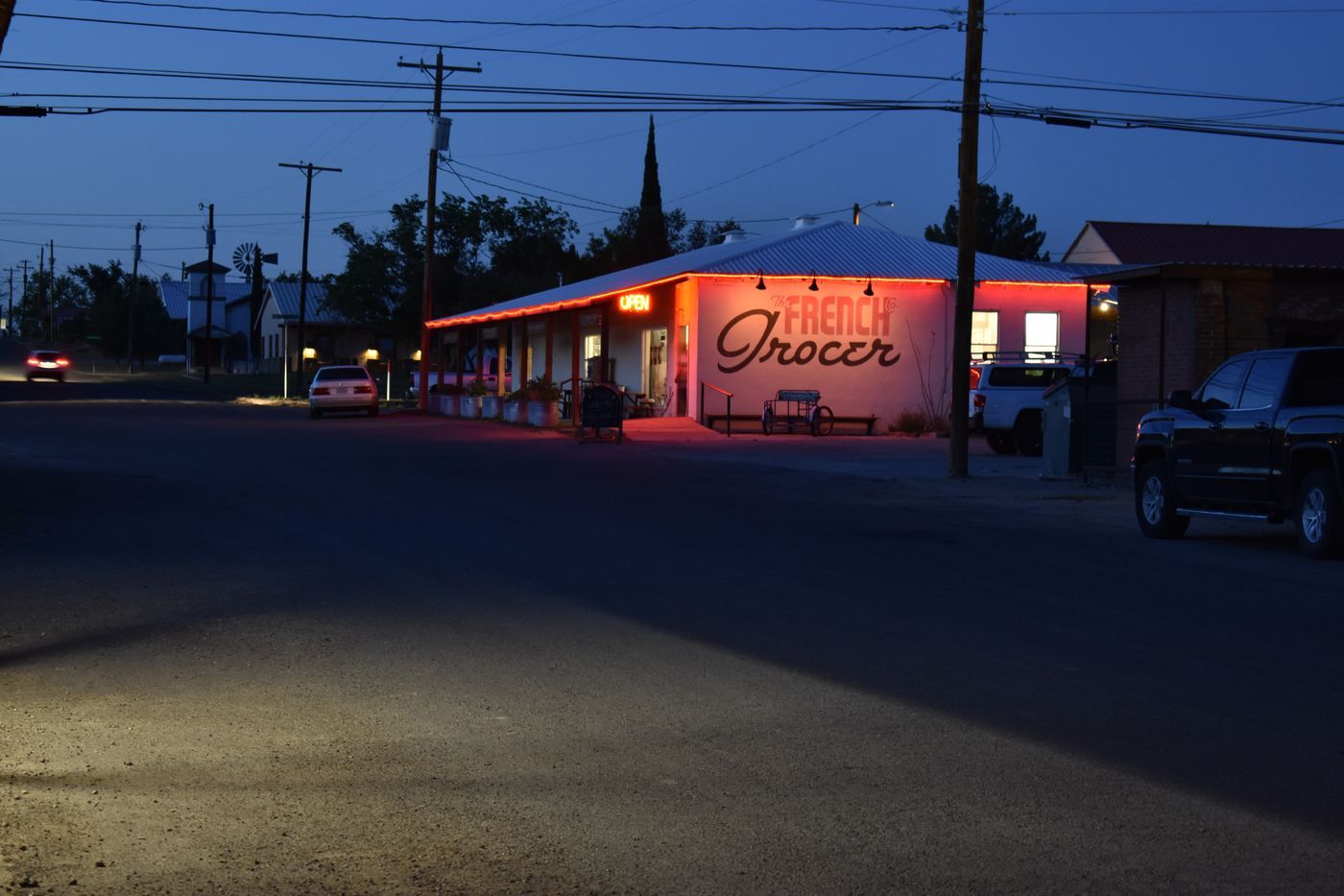The neon French Grocer sign glowing on a quiet Marathon, Texas street corner at dusk
