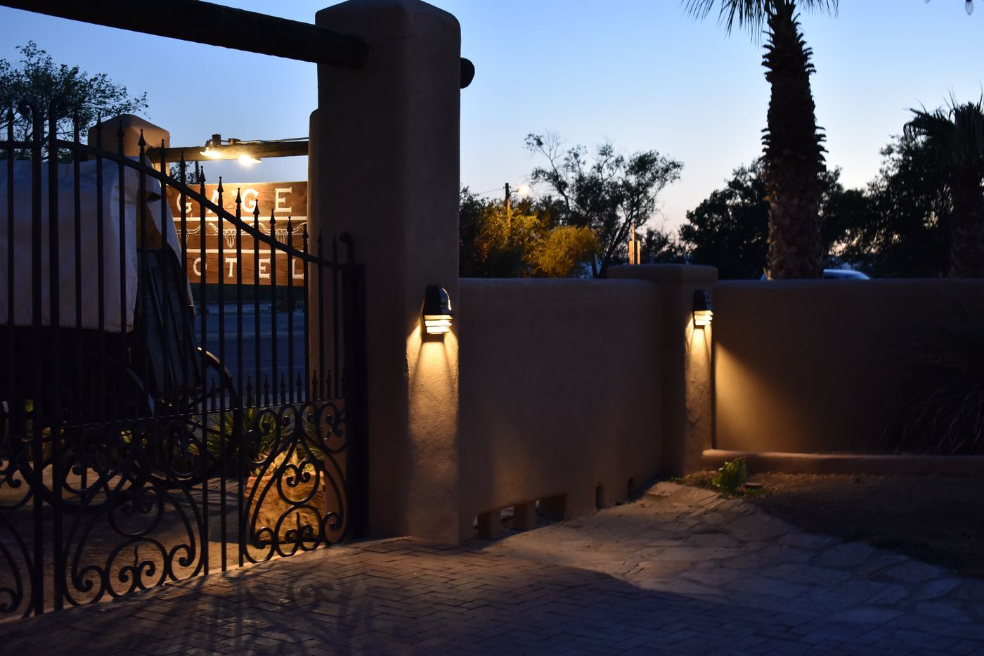 The lit adobe entrance wall and iron gate of the Gage Hotel in Marathon, Texas, at dusk
