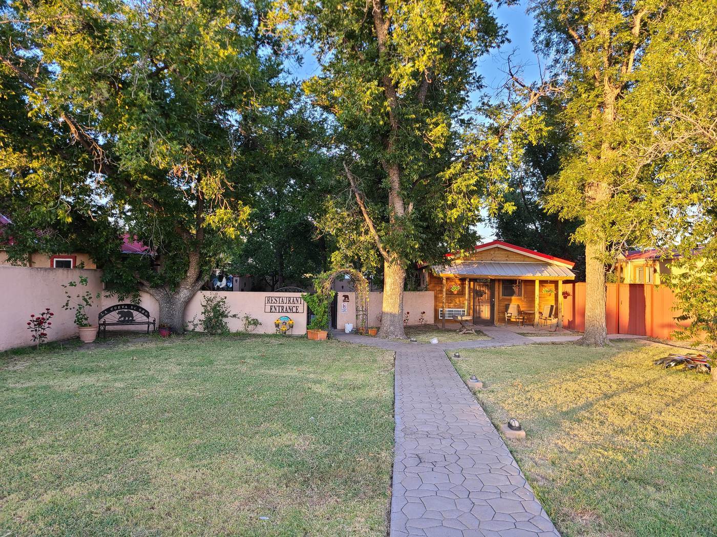 A low building set back among large shade trees with a lawn and walkway leading up to the entrance