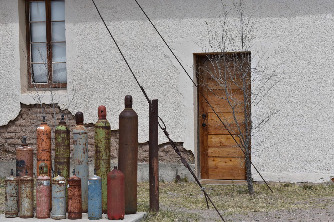 A row of old painted gas cylinders lined against a white stucco wall beside a wooden door in Marfa, Texas
